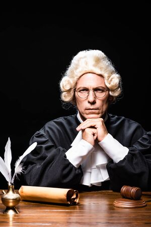 serious judge in judicial robe and wig looking at camera isolated on blackの写真素材