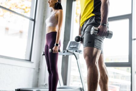 cropped view of sportsman and sportswoman working out with dumbbells in sports centerの写真素材