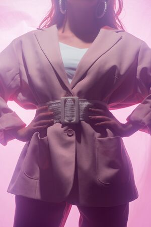 cropped view of woman standing with hands on hips on pink