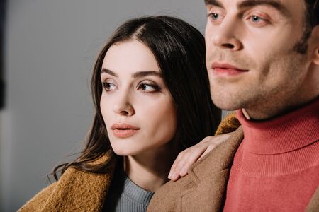 portrait of stylish couple posing in beige coats, isolated on grey