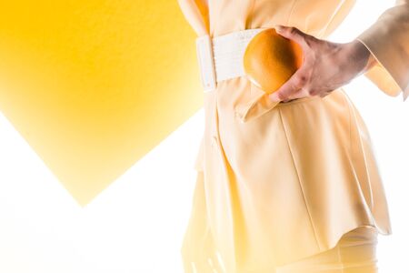 cropped view of stylish woman holding orange on white and yellow