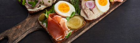 panoramic shot of tasty smorrebrod sandwiches on wooden cutting board on grey surface