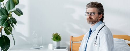 panoramic shot of handsome doctor in white coat looking at camera in hospitalの写真素材