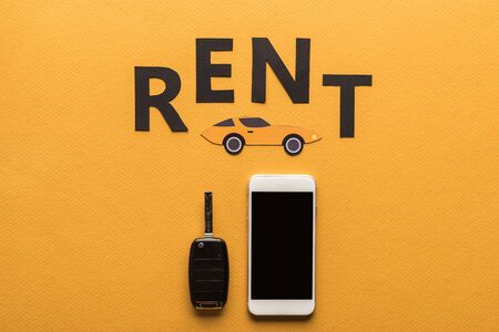 top view of smartphone with blank screen, car key, paper cut auto and black rent lettering on orange backgroundの写真素材