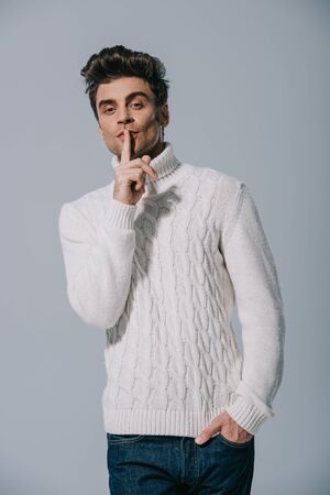 happy man in white knitted sweater showing silence symbol, isolated on greyの写真素材