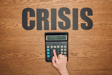 cropped view of female hand on calculator with one hundred thousand on display, and word crisis on wooden deskの写真素材