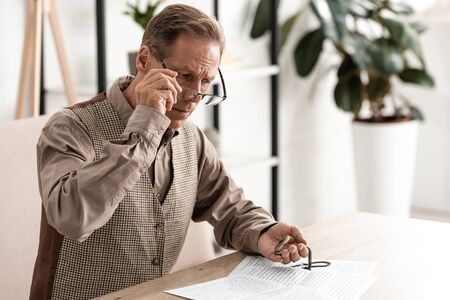 senior man holding compass while touching glassesの写真素材