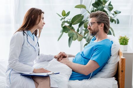 doctor in white coat holding hand and looking at patient in hospitalの写真素材