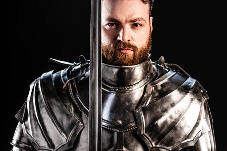 handsome knight in armor holding sword isolated on blackの写真素材