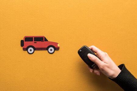 cropped view of woman holding key near paper cut car on orange background