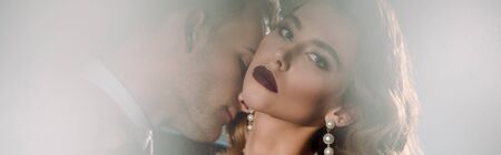 panoramic shot of attractive woman looking at camera near handsome gangster on white