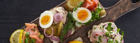 panoramic shot of wooden cutting board with fresh danish smorrebrod sandwiches on grey surface