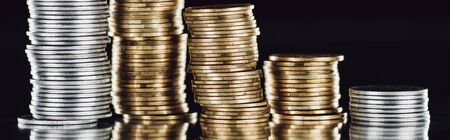 panoramic shot of stacked silver and golden coins on surface with reflection isolated on black