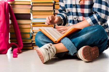 cropped view of schoolkid sitting near books and pink backpack on white