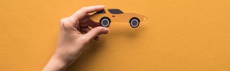 cropped view of woman holding paper cut sports car on orange background, panoramic shotの写真素材