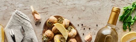 top view of delicious served escargots near bottle of white wine and ingredients on stone background, panoramic shotの写真素材