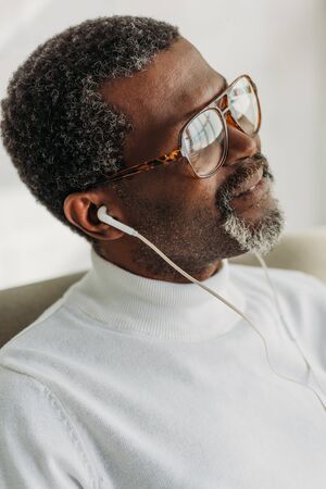 dreamy african american man in glasses listening music in earphones