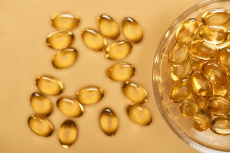 top view of shiny golden fish oil capsules scattered from glass bowl on yellow backgroundの写真素材
