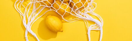 top view of fresh ripe whole lemons in eco string bag on yellow background, panoramic shotの写真素材