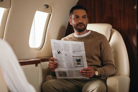 selective focus of bearded man holding newspaper in private jet