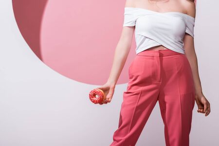 cropped view of woman holding doughnut on pink and white
