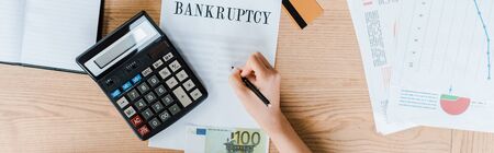 panoramic shot of businesswoman using calculator near euro banknote and document with bankruptcy...