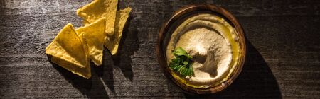 top view of delicious hummus with corn nachos on wooden rustic table, panoramic shot