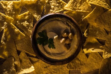 top view of delicious hummus with chickpeas in bowl near nachosの写真素材