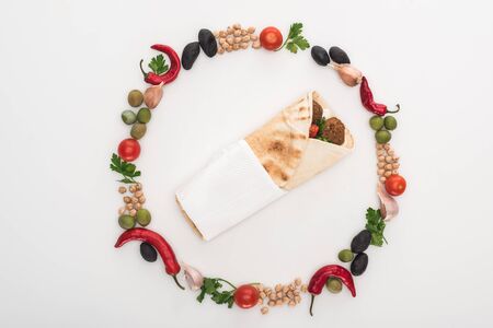 top view of chickpea, garlic, cherry tomatoes, parsley, olives, chili pepper, green onion arranged in round frame around falafel in pita on white backgroundの写真素材