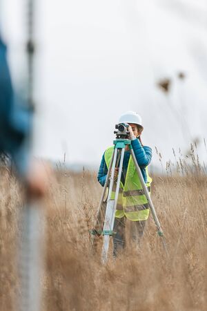 Selective focus of surveyors measuring land with digital level and ruler in field