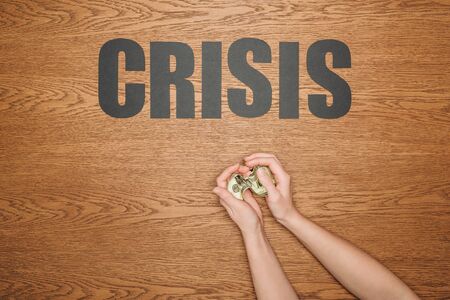 cropped view of female hands with dollar banknote near black paper cut word crisis on wooden deskの写真素材