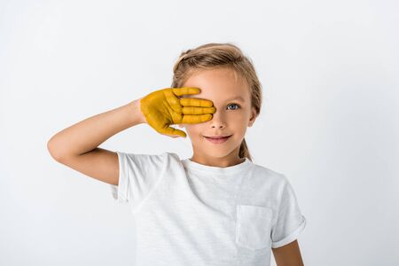 happy kid with yellow paint on hand covering face isolated on whiteの写真素材