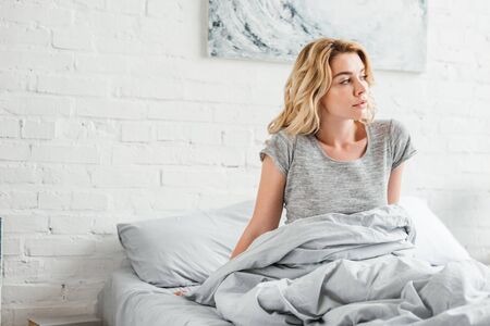 beautiful young woman sitting on bed at homeの写真素材