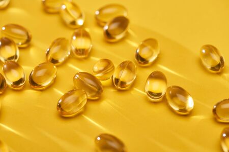 close up view of golden shiny fish oil capsules scattered on yellow bright backgroundの写真素材