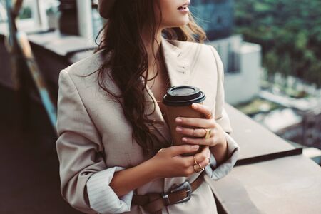cropped view of fashionable girl in beige suit posing on roof with coffee to goの写真素材