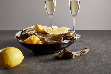 selective focus of delicious oysters and lemons in bowl near champagne glasses with sparkling wine...