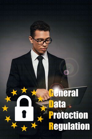 african american businessman using laptop on dark background with gdpr illustration