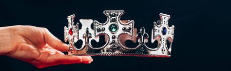 cropped view of woman holding silver crown with gemstones, isolated on black, panoramic shotの写真素材