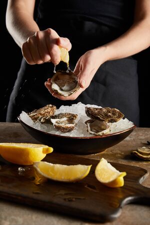 selective focus of woman squeezing lemon on oyster isolated on blackの写真素材