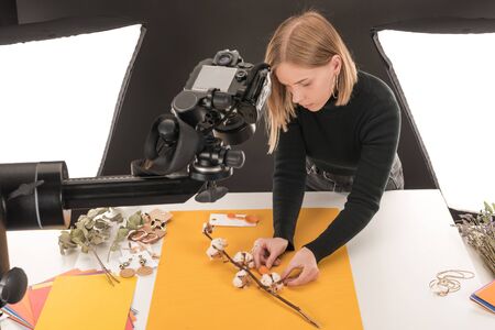 young photographer making composition with cotton flower and accessories for photo shooting