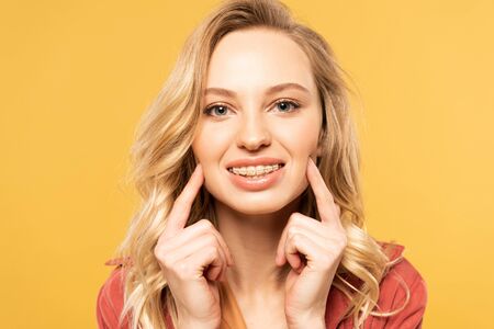 Smiling blonde woman with dental braces looking at camera isolated on yellowの写真素材