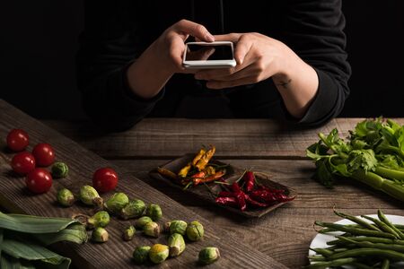 cropped view of professional photographer making food composition for commercial photography on smartphone on wooden tableの写真素材