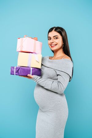 smiling pregnant pretty girl holding presents isolated on blueの写真素材