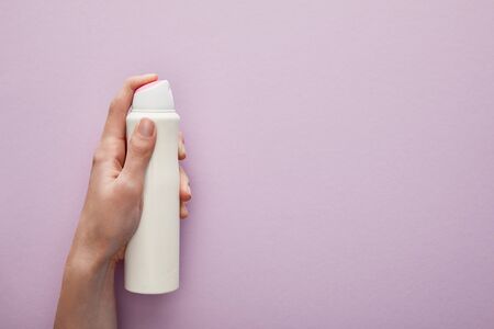cropped view of woman holding spray deodorant on violet background with white rosesの写真素材