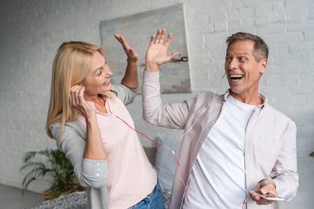 Smiling couple in earphones giving high five while listening music