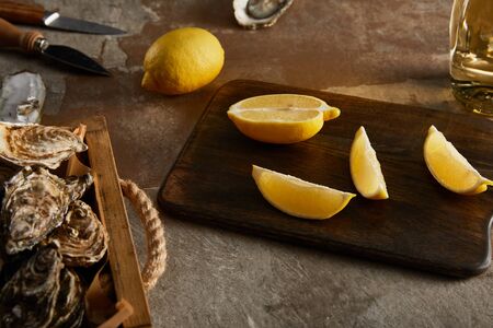 selective focus of delicious oysters in shells near lemons on wooden cutting board