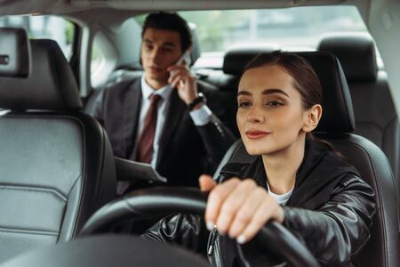 Woman taxi driver holding steering wheel while businessman talking on smartphone