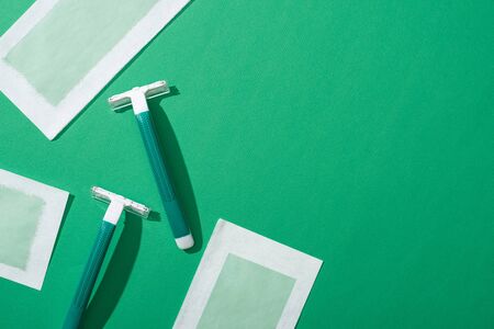 top view of green disposable razors and depilation wax stripes on green background