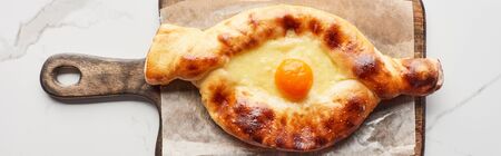 Top view of adjarian khachapuri on chopping board on marble texture, panoramic shot