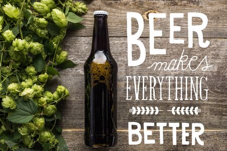 top view of fresh beer in bottle with green hop on wooden surface with white beer makes everything better illustrationの写真素材